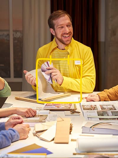 Ein IKEA Interior Designer berät eine Gruppe von Kunden an einem Tisch mit Hilfe von Prospekten, Zeichnungen und Farbkarten