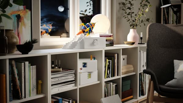 Ein IKEA KALLAX Regal mit Büchern und Deko und obendrauf eine Rakete gebaut aus LEGO.