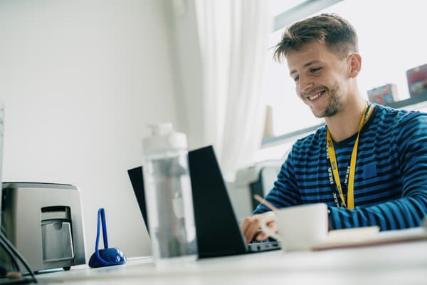 Ein IKEA Lehrling zum E-Commerce-Kaufmann sitzt am Schreibtisch vor dem Laptop und lächelt.