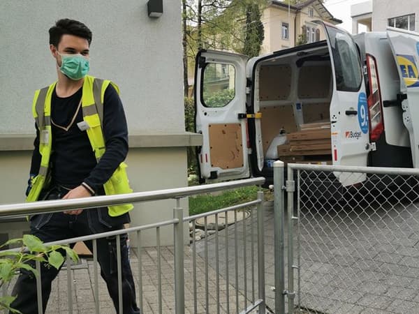Ein IKEA Mitarbeiter mit Gesichtsmaske vor einem Lieferwagen in dem neue Möbel für die Notunterkunft liegen