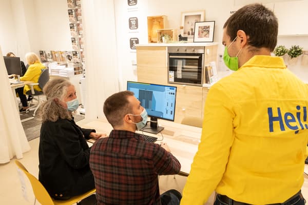 Ein IKEA Mitarbeiter schaut plant gemeinsam mit zwei Kunden an einem Computer, alle tragen Masken.