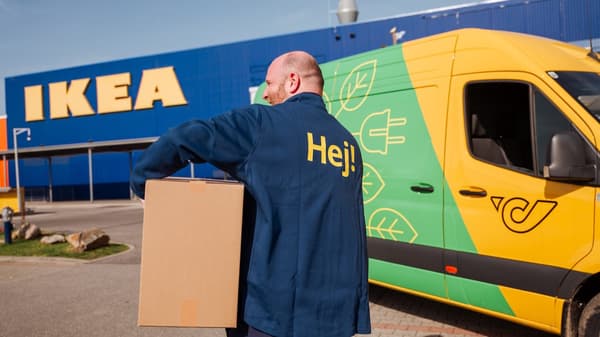 Ein IKEA Mitarbeiter trägt ein Paket und im Hintergrund steht ein Auto der Österreichischen Post