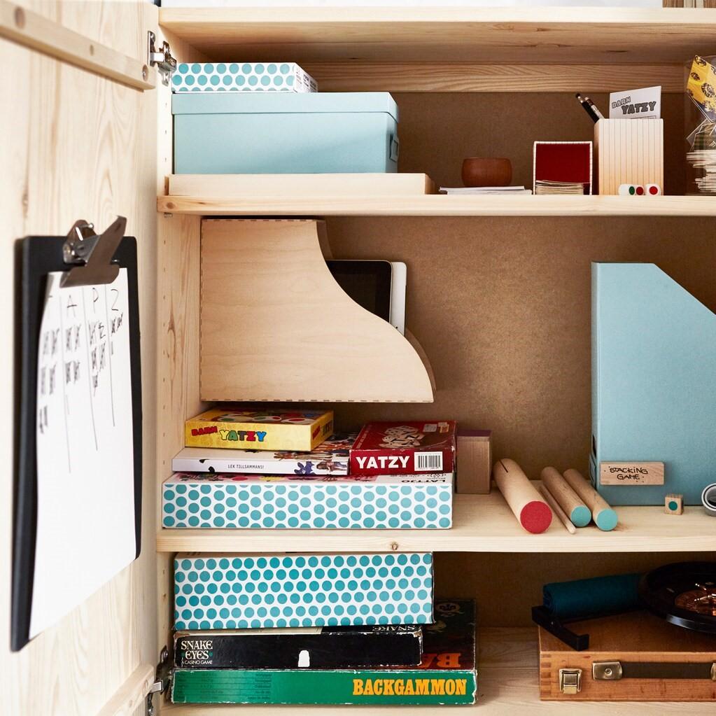 Ein IVAR Schrank Kiefer als Aufbewahrung für Brettspiele und Unterhaltungsmedien mit Körben für Controller, Haken für Kopfhörer und Zeitschriftensammler als Aufbewahrung.