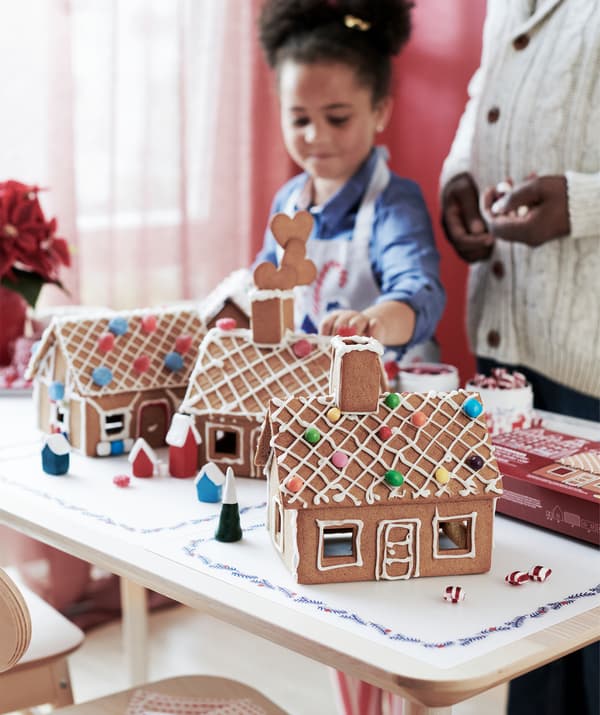 Ein Kind und eine erwachsene Person stehen an einem Tisch vor mehreren fertigen VINTERSAGA Pfefferkuchenhäusern, die schon fertig dekoriert sind.