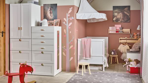 Ein Kinderschlafzimmer in Weiß/Rosa mit einem Kleiderschrank und einem Babybett mit Betthimmel in Weiß.