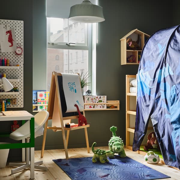Ein Kinderzimmer mit einem KURA umbaufähigen Bett, einem Baldachin, Dinostofftieren, einem Schreibtisch, einer grünen Hängeleuchte und einem blauen Teppich