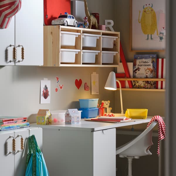 Ein Kinderzimmer mit einem weißen LÄRANDE Schreibtisch mit Auszug unter einem TROFAST Regalrahmen zur Befestigung an der Wand mit weißen Boxen.
