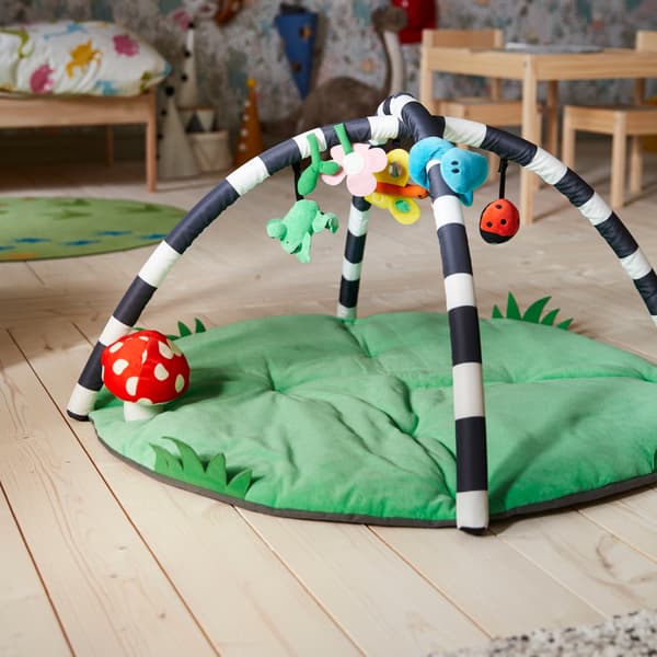 Ein KLAPPA Babygymnastikcenter auf Holzboden. Dahinter sind ein Kinderbett und ein Tisch zu sehen.