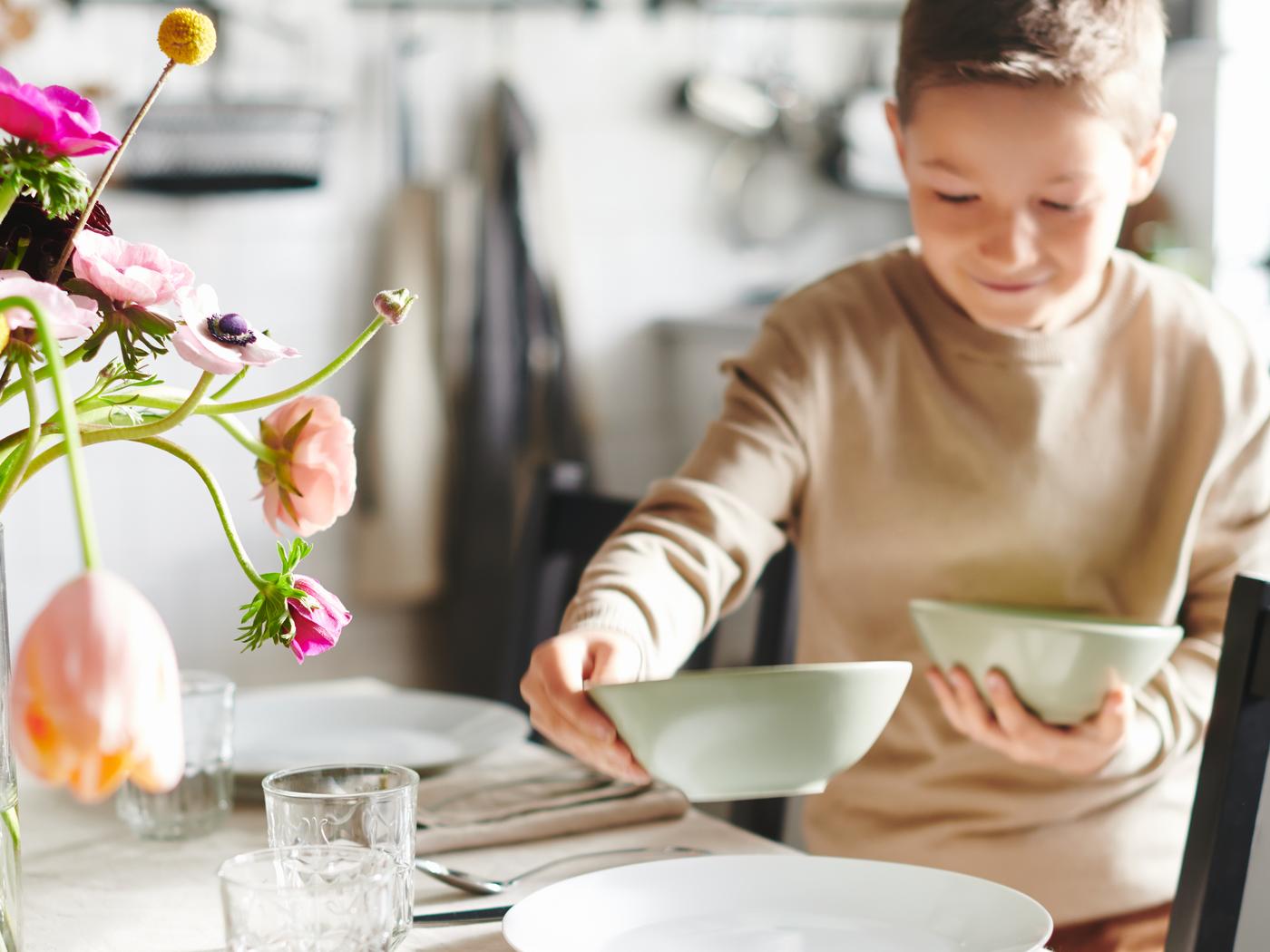 Ein kleiner Junge stellt zwei Schüsseln auf einen Tisch für den Muttertag.