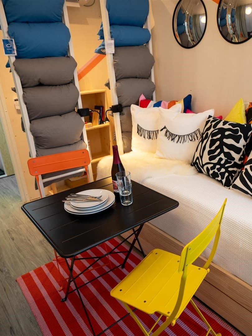 Ein kleiner Raum mit Klappstühlen und einem Klapptisch, dahinter das aussziehbare GLAMBERGET Bett.