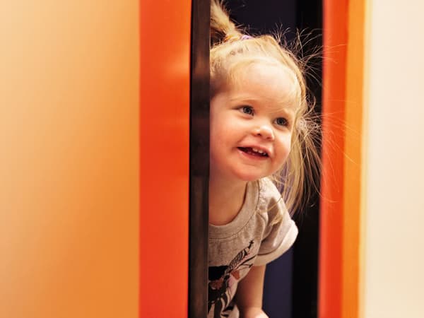 Ein kleines Mädchen schaut von einer Wand hervor und lacht
