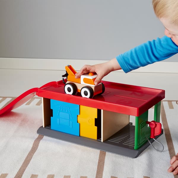 Ein Kleinkind spielt mit der bunten IKEA LILLABO Tankstelle mit Abschleppwagen auf dem Fussboden.