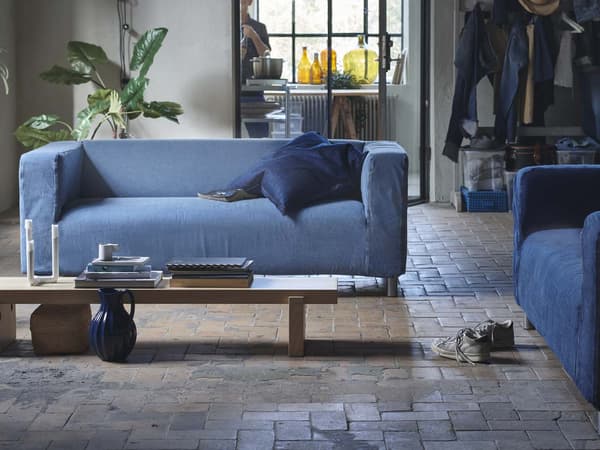 Ein KLIPPAN 2er Sofa mit grauem Bezug. Davor schwarze LACK Couchtische. An der Wand dahinter hängen bunte Skizzen und Bilder. 