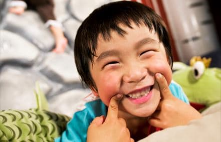Ein lachendes Kind spielt fröhlich mit einem grünen Plüschtier. Der Moment voller Lebensfreude vermittelt Spaß und Unbeschwertheit im Kinderzimmer.

