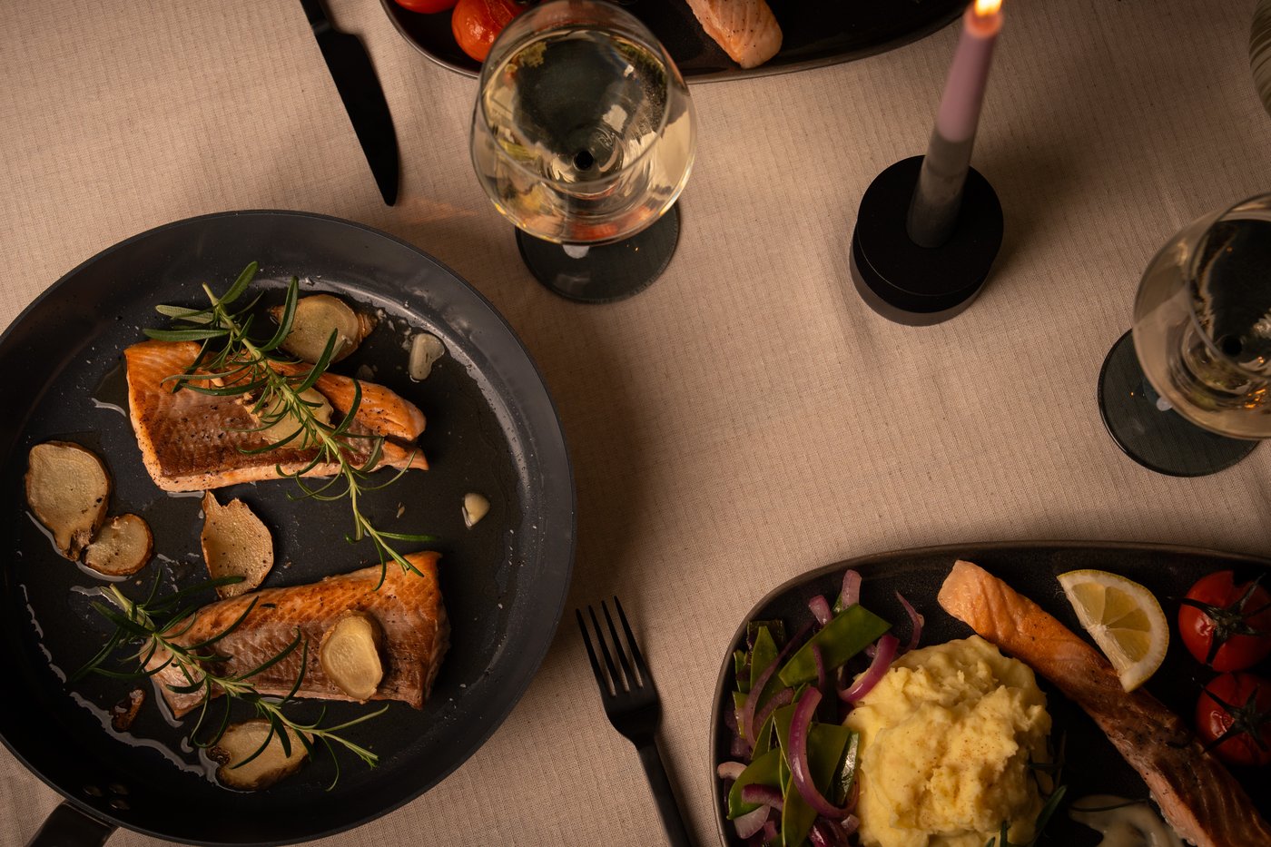 Ein Lachs mit Kartoffelpüree, Senfsauce und Gemüse auf einem dunklen Teller präsentiert.