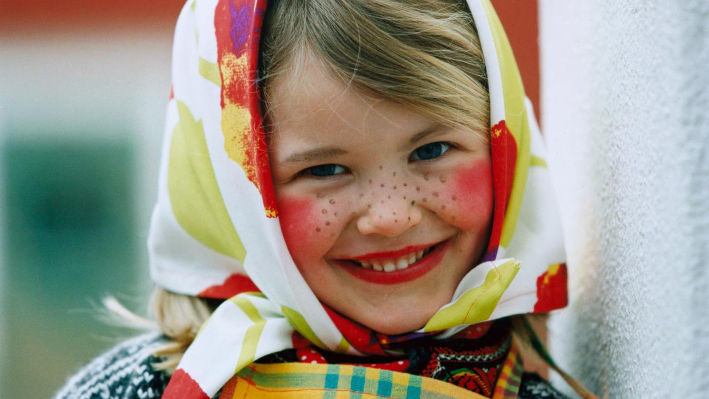Ein lächelndes Kind, das zu einer süßen Hexe geschminkt wurde, mit roten Wangen, Sommersprossen und einem Tuch um den Kopf.