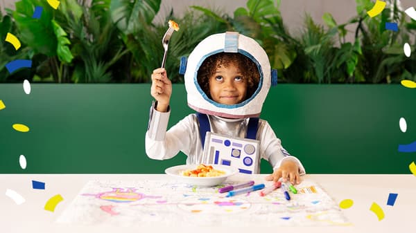Ein Mädchen in einem Astronautenkostüm isst im IKEA Restaurant ein Kindermenü.
