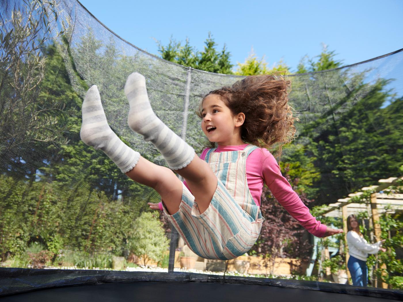 Ein Mädchen springt auf einem Trampolin im Garten.