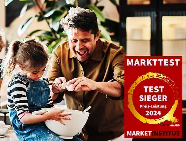 Ein Mann gibt ein Ei in eine Rührschüssel die ein Mädchen hält. Im rechten unteren Eck im Bild sieht man das Markttest Testsieger Logo für das Jahr 2024.