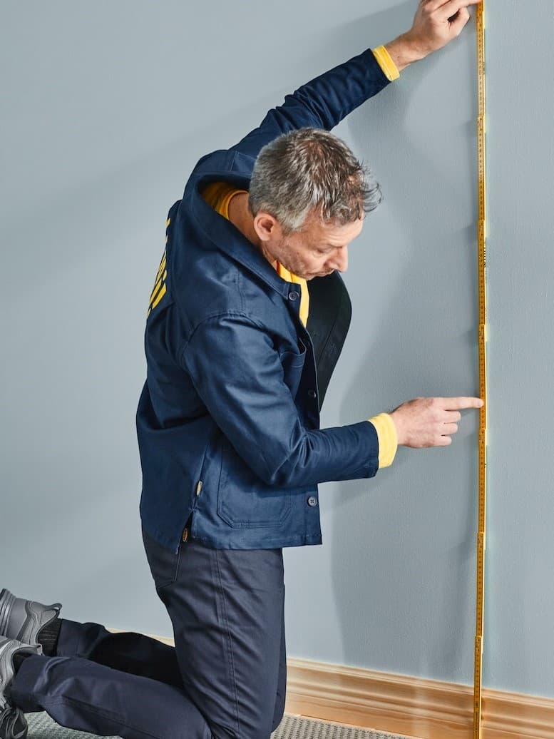 Ein Mann misst eine Wand mit Hilfe eines Zollstockes aus.