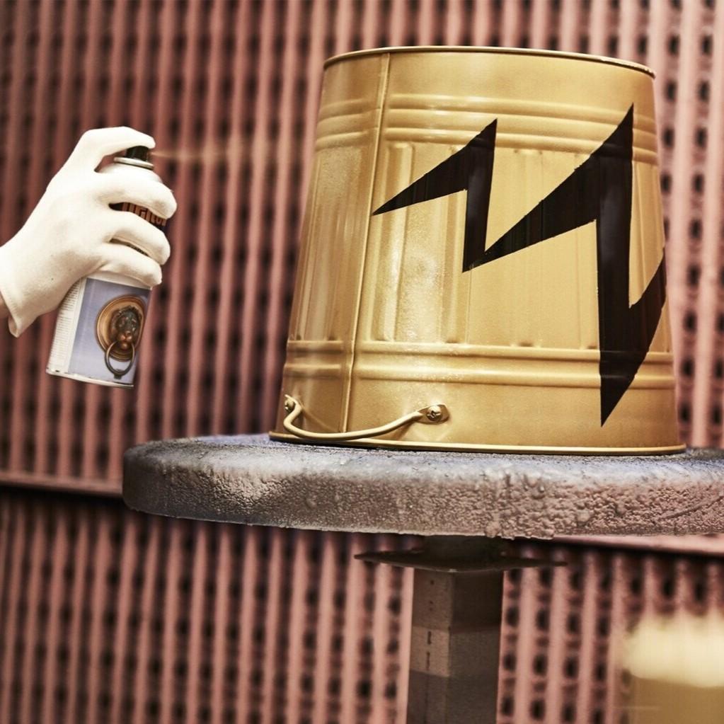 Ein Mann sprüht ein Muster auf einen goldenen Eimer mit schwarzer Farbe.