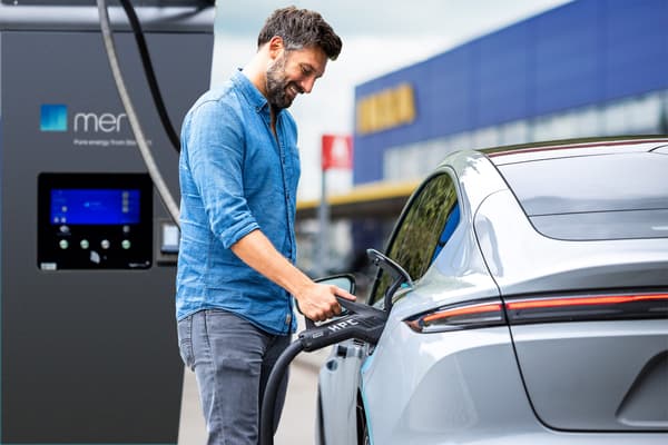 Ein Mann steht an einer E-Ladestation und lädt sein Auto.