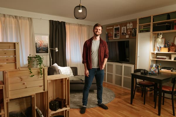 Ein Mann steht in einem Raum und im Hintergrund sieht man ein kleines Wohnzimmer