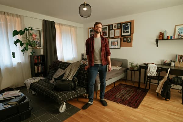 Ein Mann steht in einem Raum und im Hintergrund sieht man ein Schlafsofa