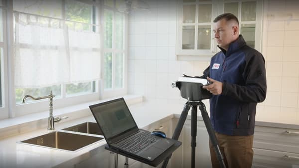 Ein Mann steht in einer Küche und nimmt mit einem Digitalen Gerät die Raummaße die auch direkt auf einen Laptop transferiert werden.
