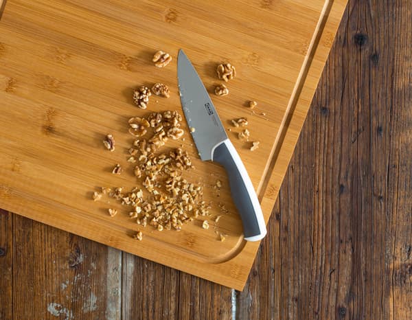 Ein Messer liegt neben gehackten Walnüssen auf einem Holzbrett.