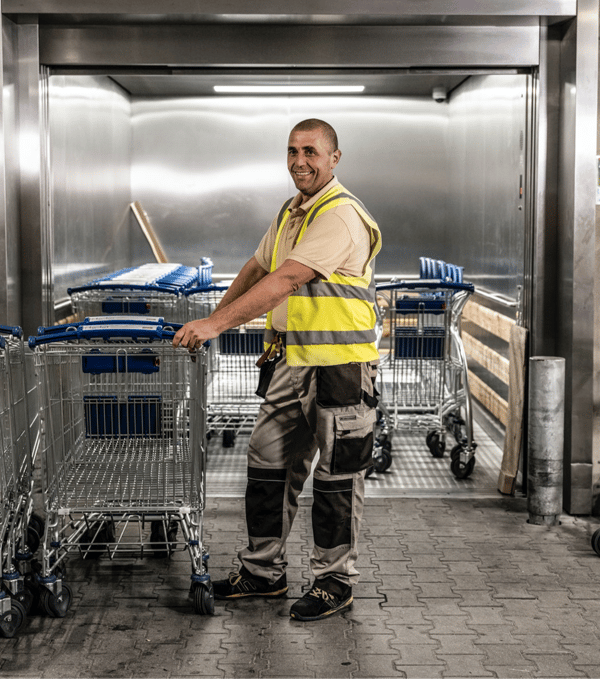 Ein Mitarbeiter in Warnweste steht an einem Tor mit Einkaufswagen.