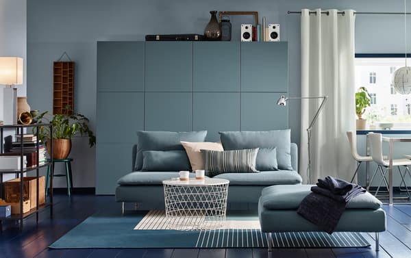 Ein mittelgroßes Wohnzimmer mit türkisem 3-Sitz Sofa mit passendem Hocker kombiniert mit einem weißen Couchtisch mit Stauraumfunktion und einer großen Aufbewahrungslösung in passendem grau-türkis.