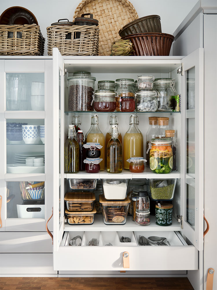 Ein offener Schrank mit Regalen und einer Schublade, in denen Vorräte ordentlich und nachhaltig in Vorratsbehältern sortiert sind.