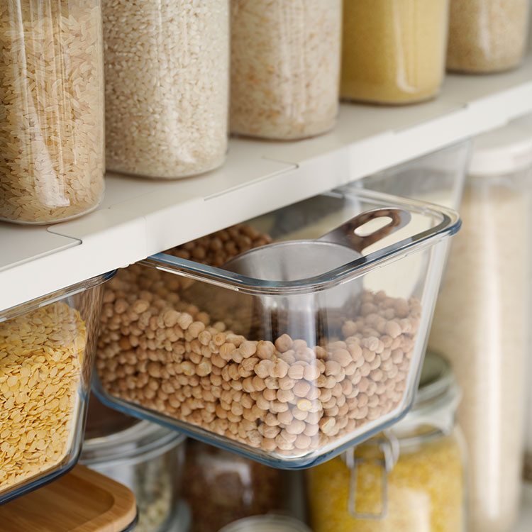 Ein offener Schrank mit Regalen und Einschubfächern, in denen Vorräte ordentlich und nachhaltig in Glasbehältern sortiert sind.