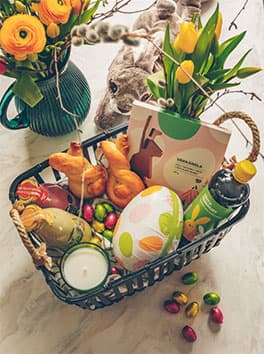 Ein Osterkorb gefüllt mit Osterschokolade, Süßigkeiten und Getränken.