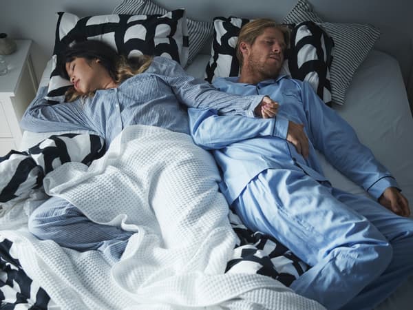 Ein Pärchen schläft gemütlich eingehüllt in Decken und Kissen in einem Bett. 