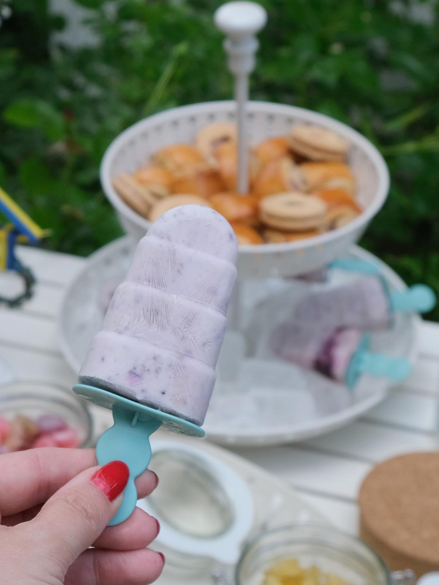 Ein Person hält ein Blaubeer-Eis über einen Tisch.