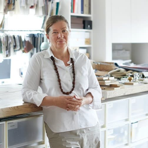 Ein Portrait der Designerin Ilse Crawford, wie sie vor einer Arbeitsfläche lehnt.