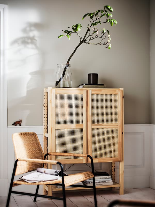 EIn Rattansessel steht vor einem Highboard aus hellem Holz mit Türen aus Holzgeflecht. 