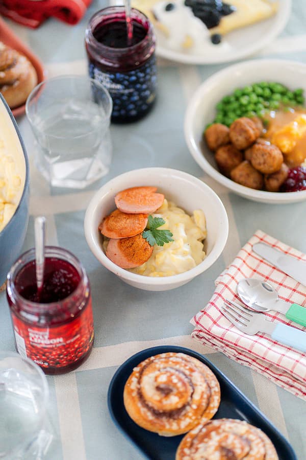 Ein reichlich gedeckter Tisch mit Zimtschnecken, Blaubeerkonfitüre und 2 kleine Schüsseln mit klassischen schwedischen Gerichten.