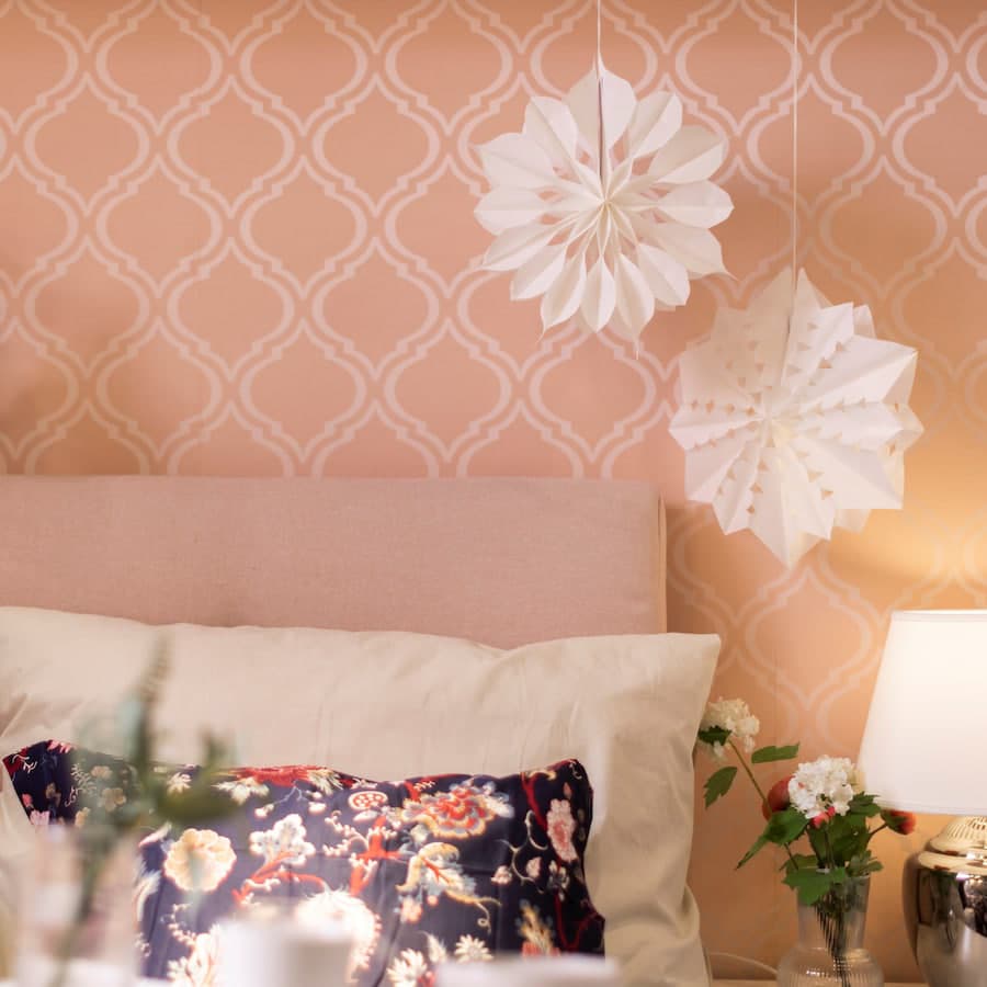 Ein rosaner Raum mit einem Bett und weißer Bettwäsche und einer weißen Tischlampe auf der rechten Seite.