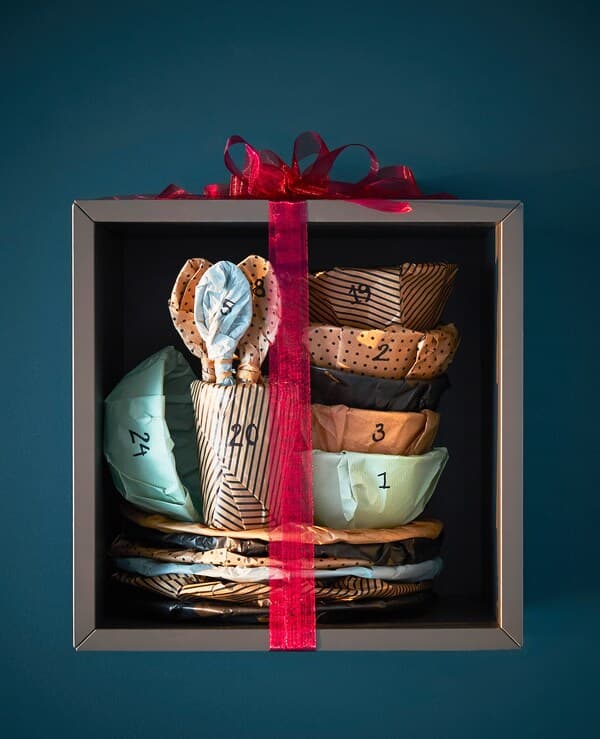 Ein Satz Besteck & Geschirr in einem Regal, festlich eingepackt mit FRAMSTÄLLA Geschenkpapierrolle