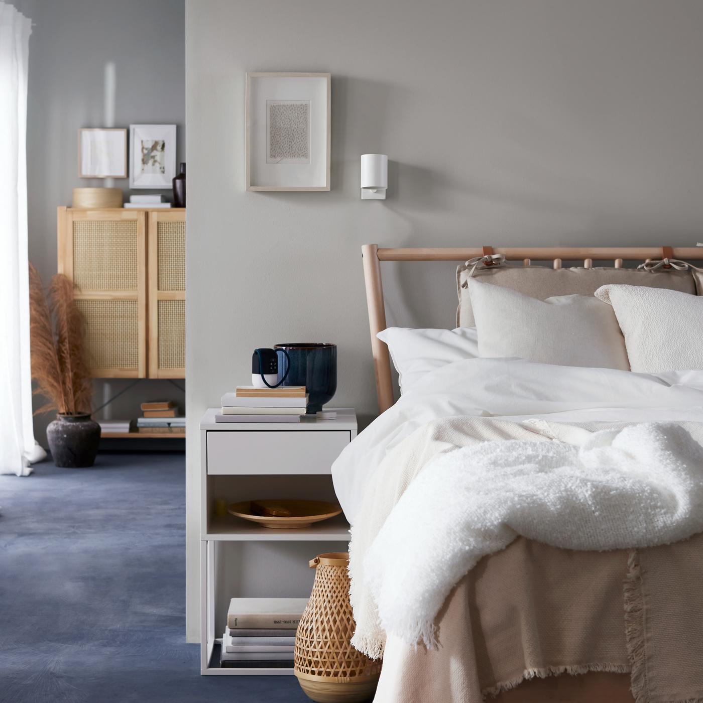 Ein Schlafzimmer mit einem hellen Holzbett ist zu sehen, das mit ÄNGSLILJA Bettwäsche bezogen ist. Darüber hängt eine weiße NYMÅNE Wand-/Leseleuchte.