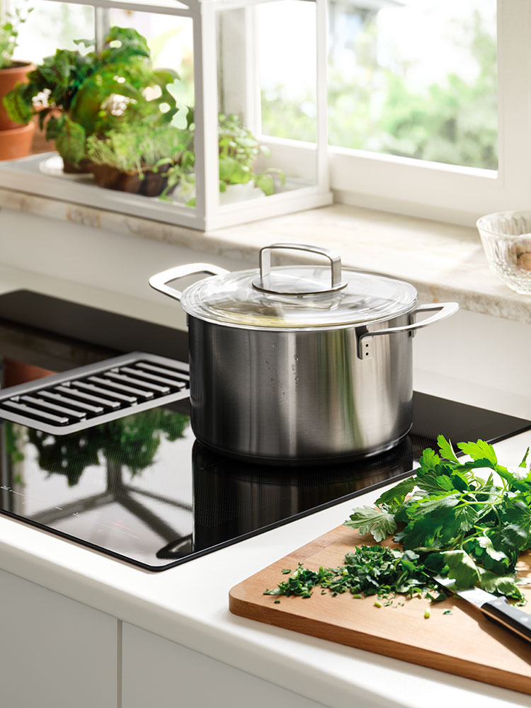 Ein Schneidebrett aus Holz liegt neben einem Kochfeld mit Topf darauf.