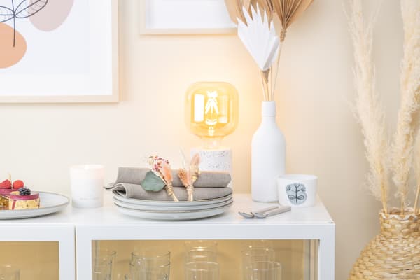 Ein selbst gebasteltes Boho-Anstecksträußchen liegt auf einem Tellerstapel mit Servietten.