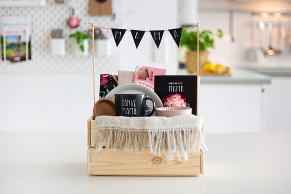 Ein selbstgebastelter Geschenkkorb aus einem KNAGGLIG Kasten zum Muttertag mit Wimpelkette, bemalter Tasse und liebevoll zusammengestellten Utensilien. 