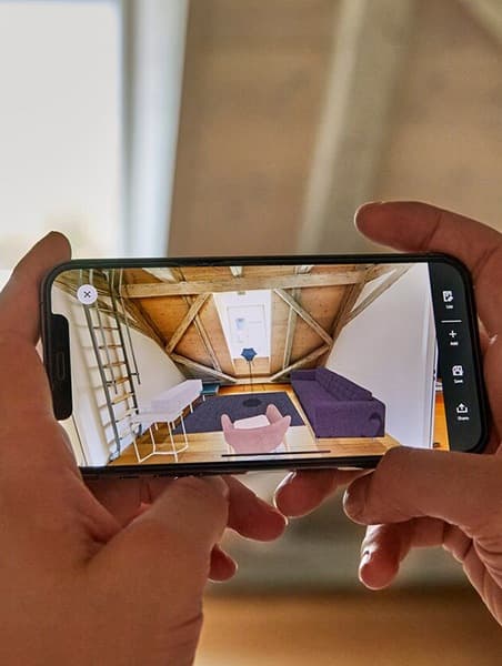 Ein Smartphone wird vor einen leeren Raum gehalten. Auf dem Bildschirm wird ein Bild gezeigt wie der Raum mit Möbeln aussieht.
