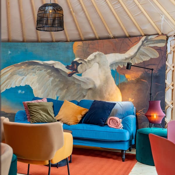 Ein Sofa mit verschiedenen Kissen steht in einer Jurte vor einer Wand mit einem raumhohen Bild eines Schwans