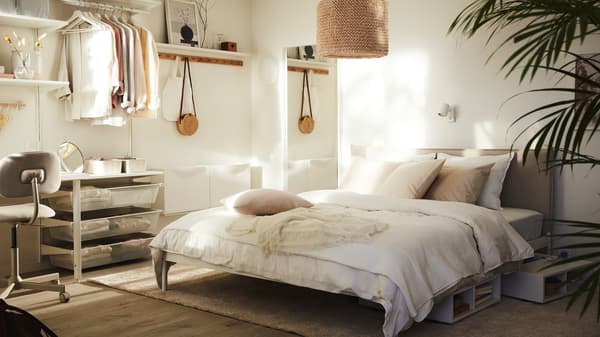 Ein sonniges, kleines Schlafzimmer in Neutralfarben mit einem KLEPPSTAD Bettgestell, heller Bettwäsche und einem LERGRYN Leuchtenschirm.
