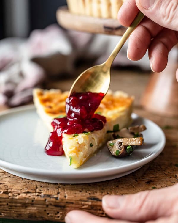 Ein Stück Midsommar Quiche mit Pilzen wird mit Preiselbeermarmelade serviert.